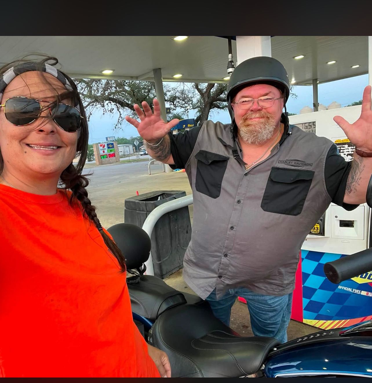 Neil waving from his motorcycle while Jamie stands nearby