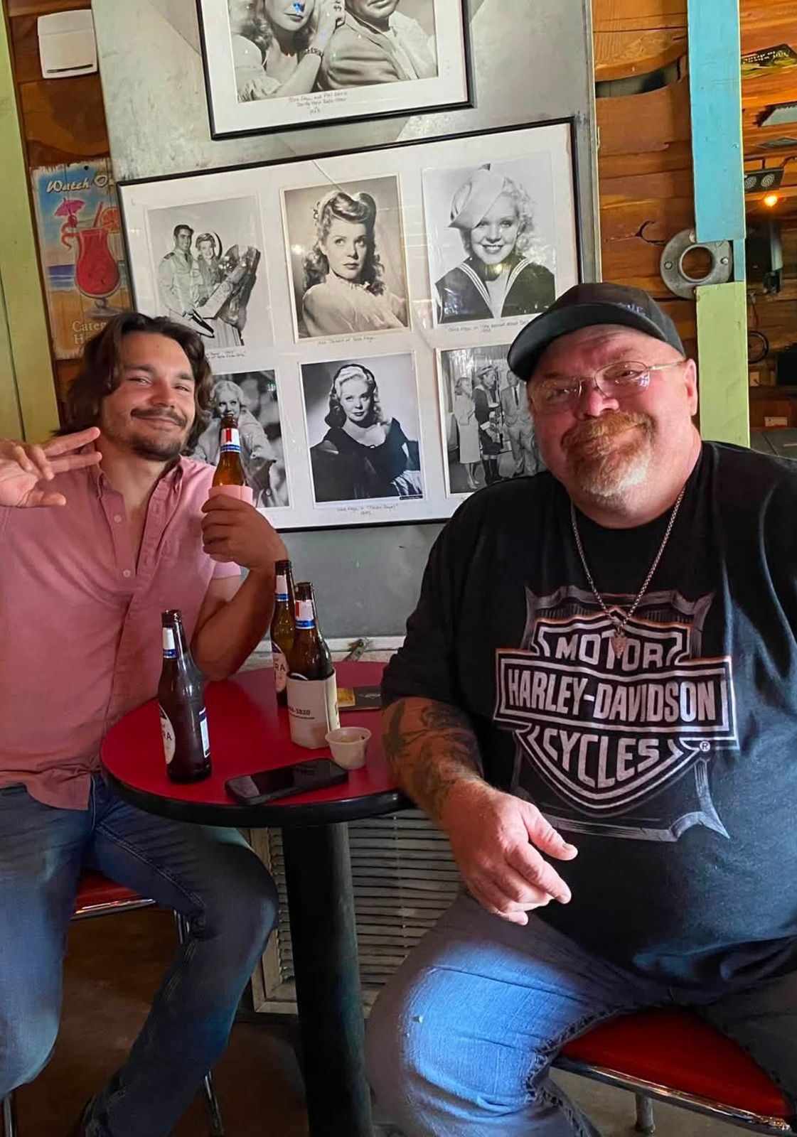 Neil at a table with a younger man, beers between them