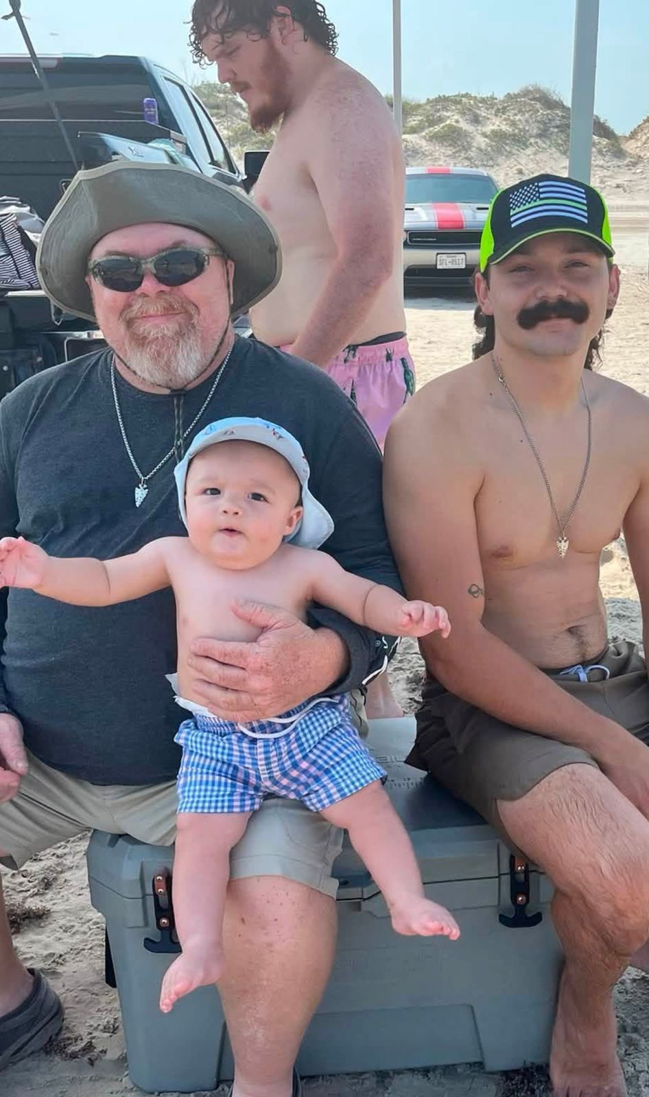 Neil on the beach holding a baby beside a younger man