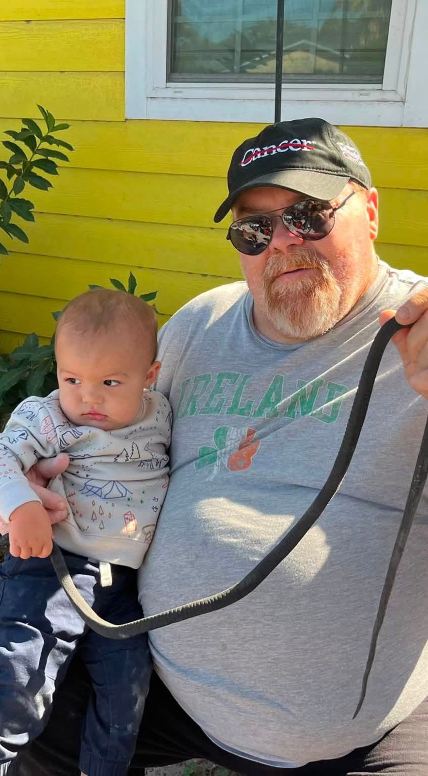 Neil outdoors in a hat and sunglasses holding a baby