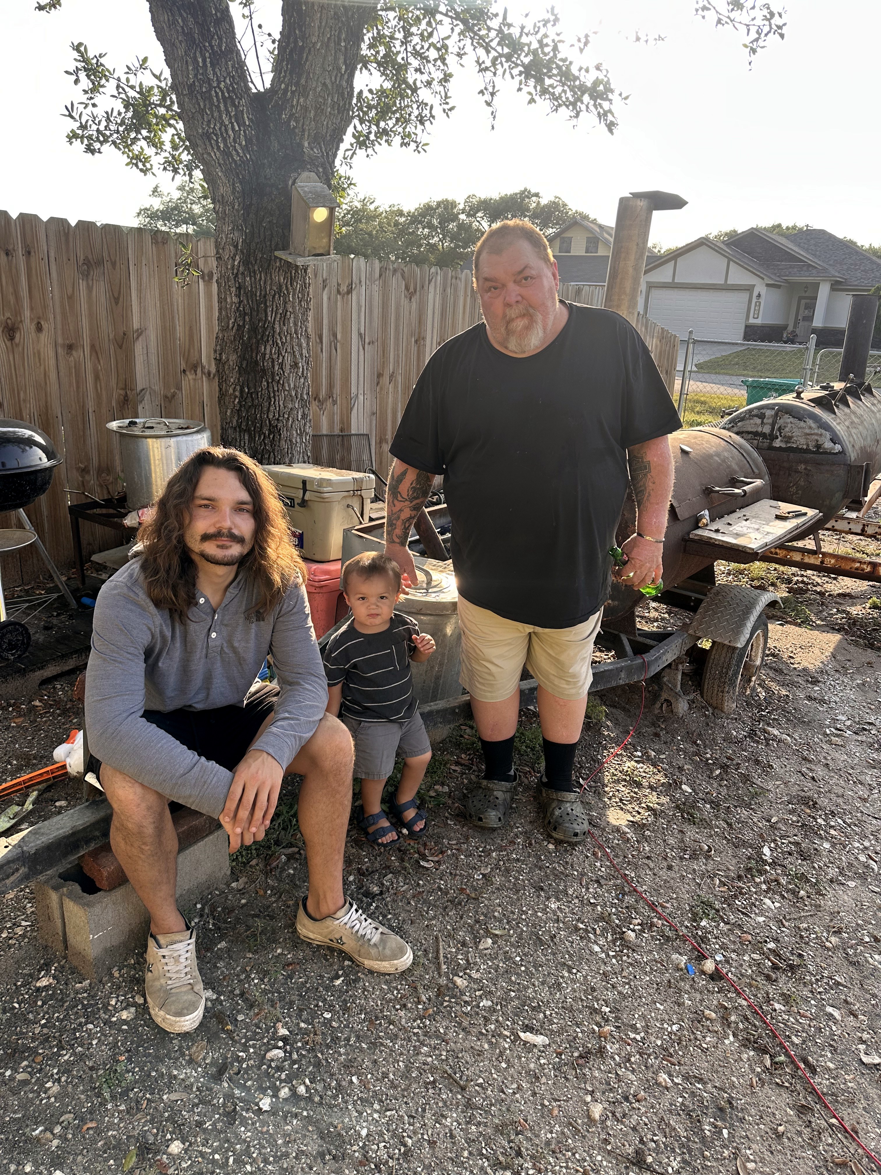 Neil by a backyard smoker with a young man and a toddler