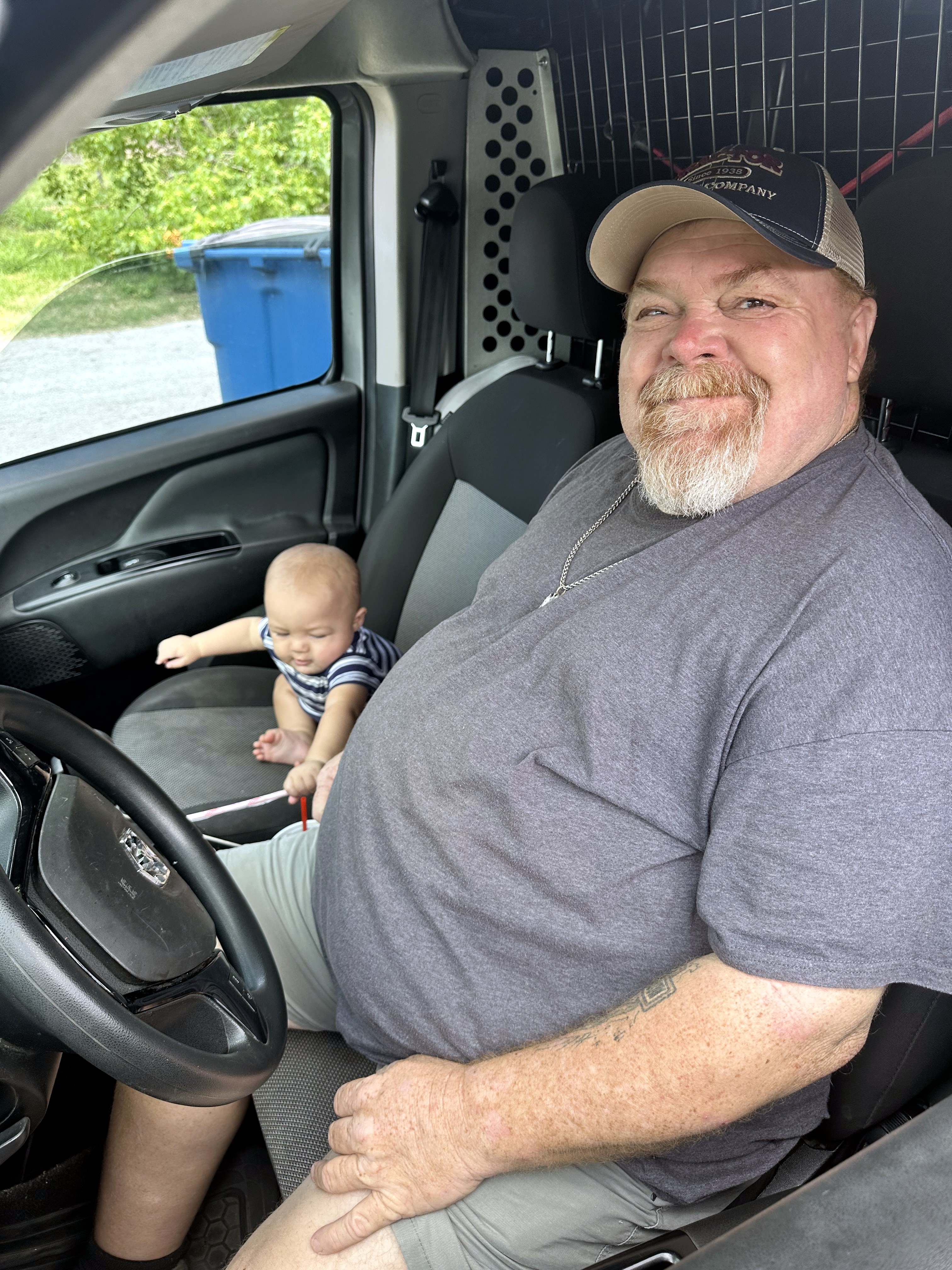 Neil smiling in a van with a baby in the passenger seat