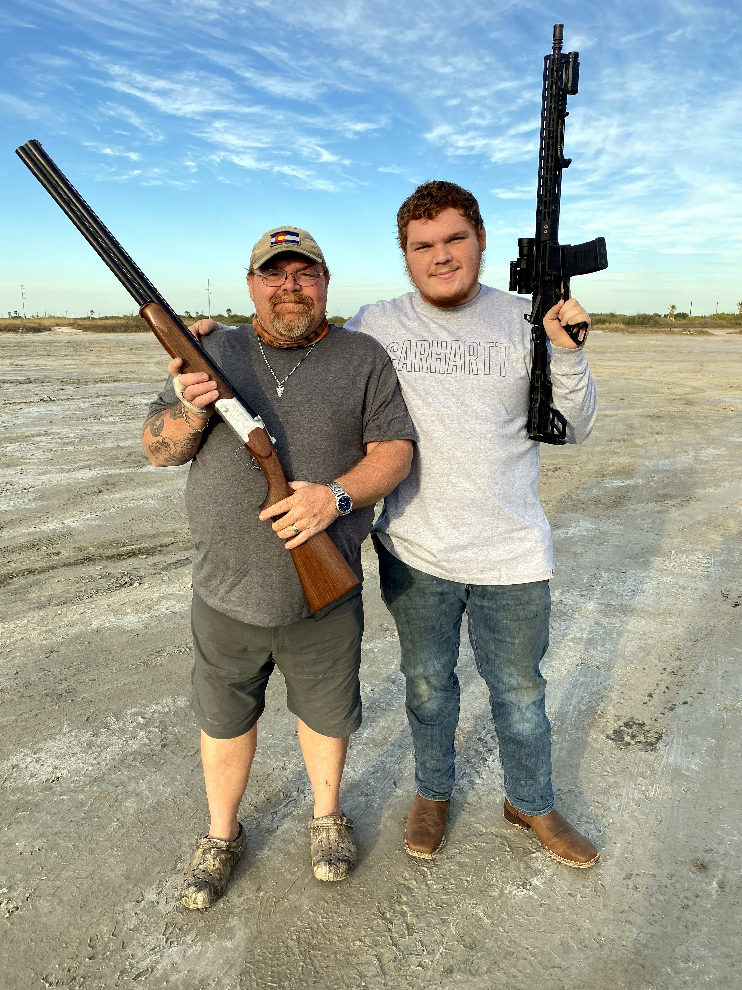 Neil and a younger man posing outdoors with firearms