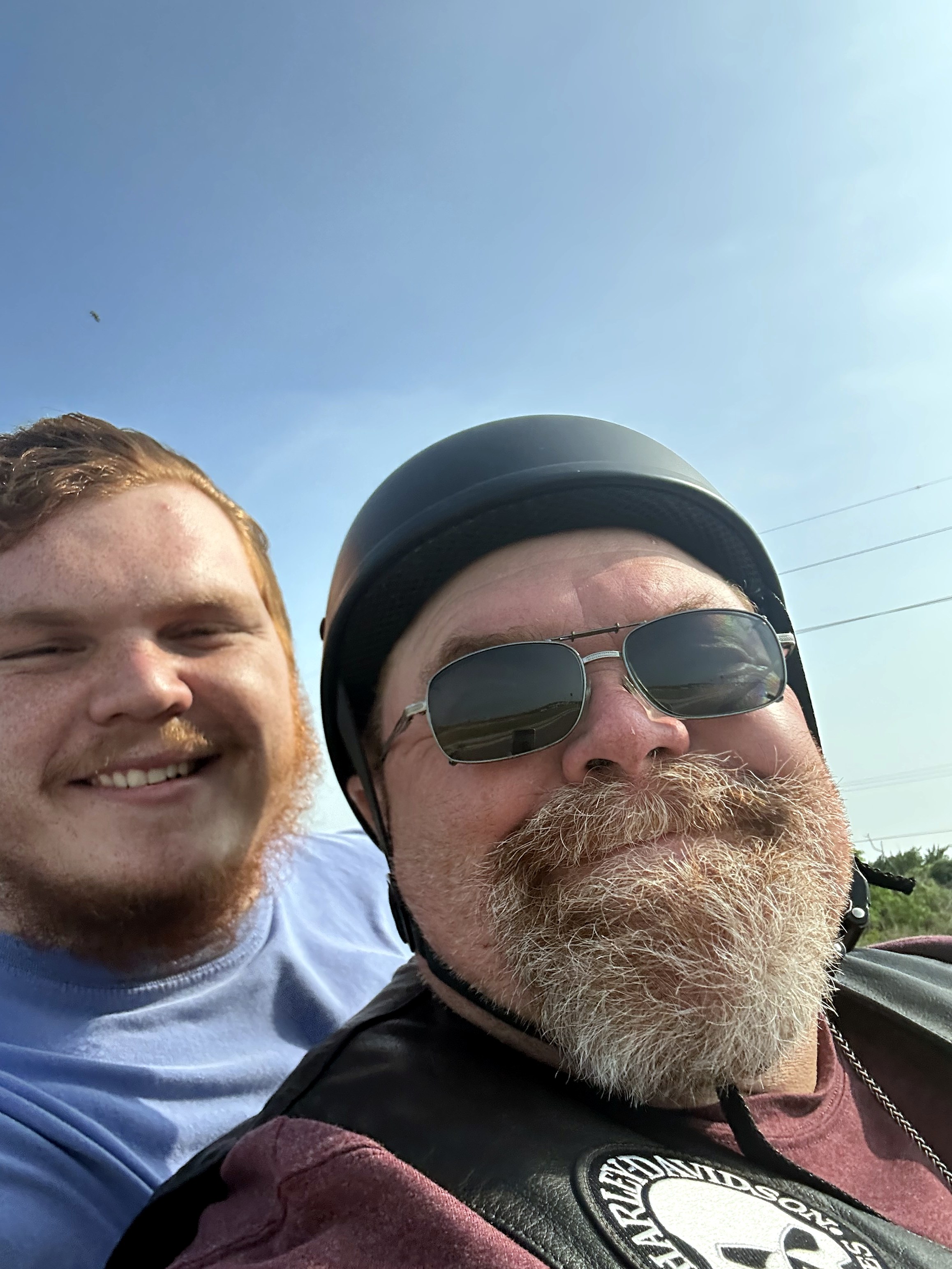 Neil in a motorcycle helmet and leather vest smiling with a friend