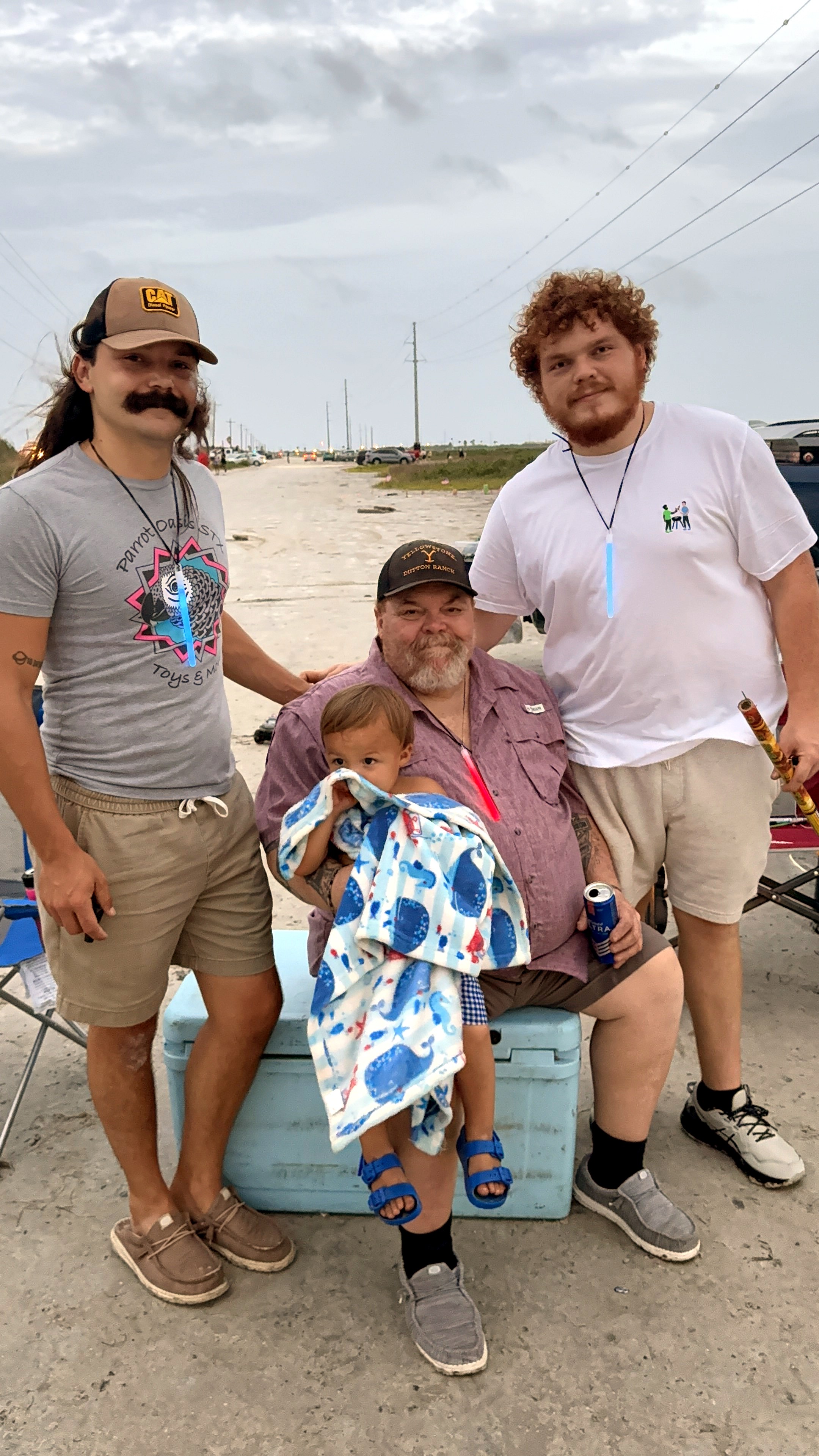 Neil seated on a cooler with a toddler and two younger men outdoors
